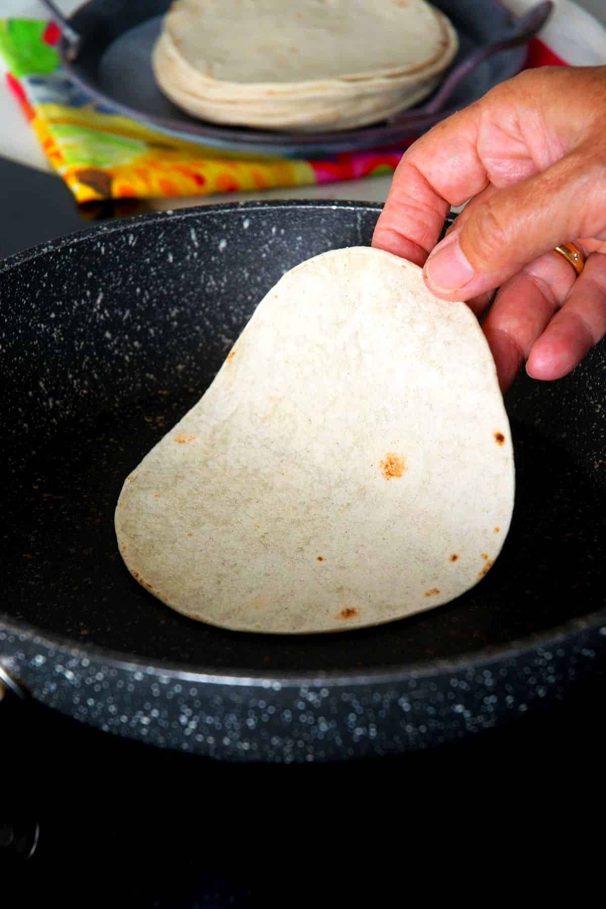 Corn tortilla placed in frying pan by woman's hand.