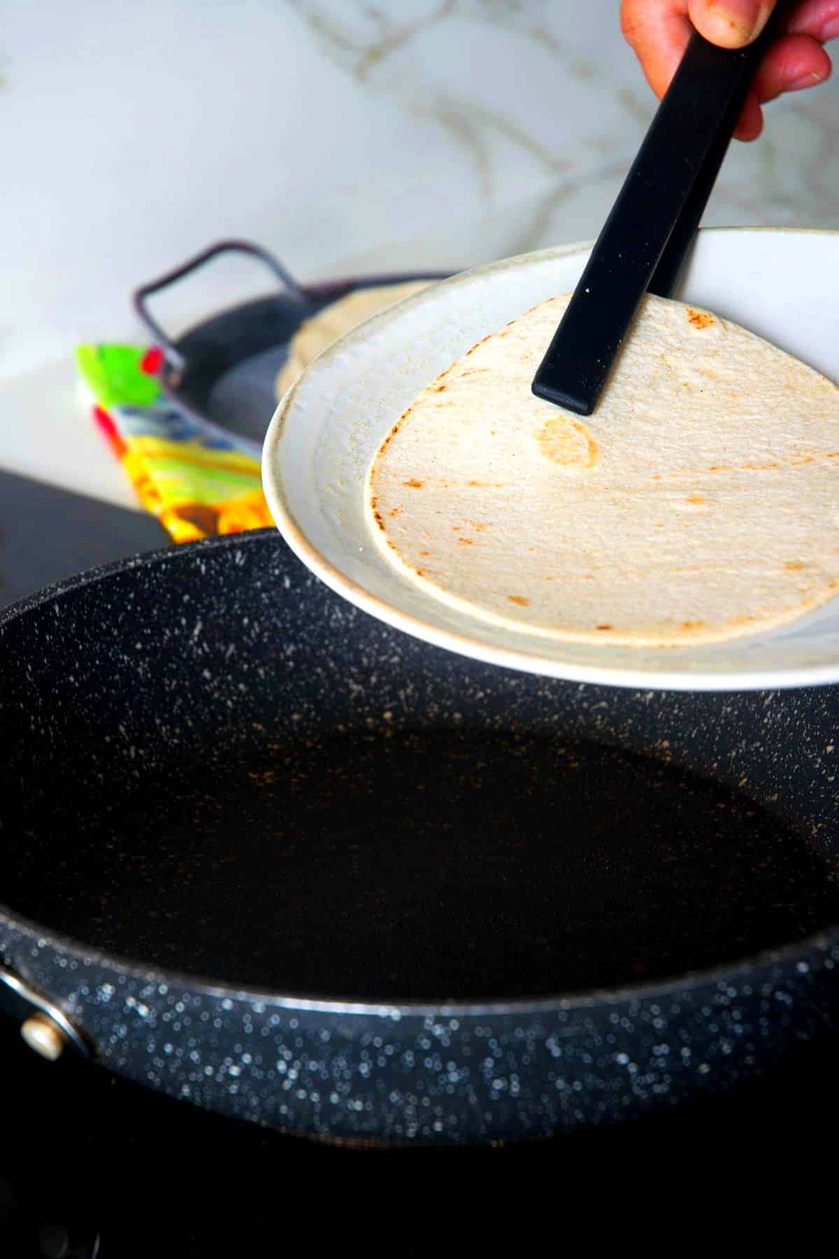 Corn tortilla removed from frying pan to plate with tongs.
