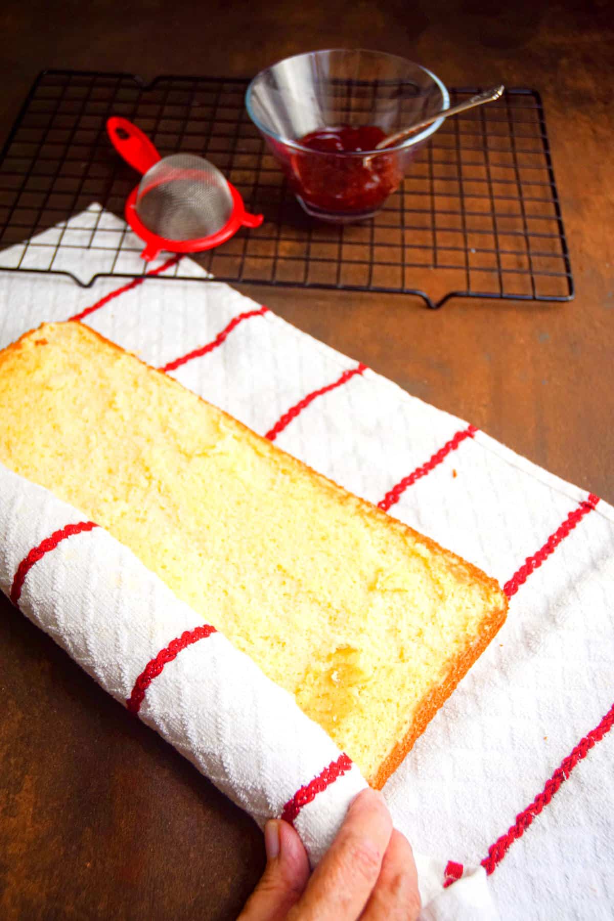 Jelly roll cake getting rolled up into towel.