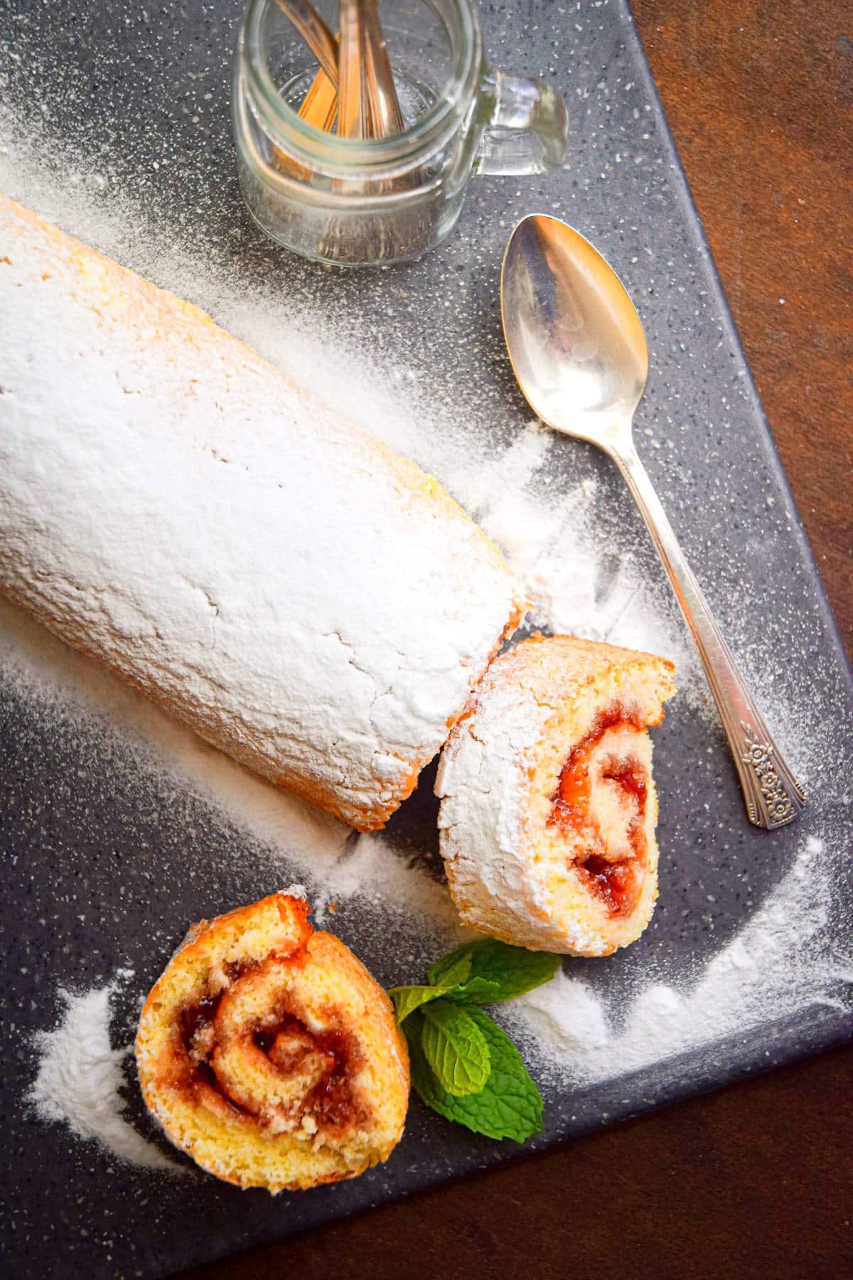 Jelly roll cake on cutting board, dusted with powdered sugar.