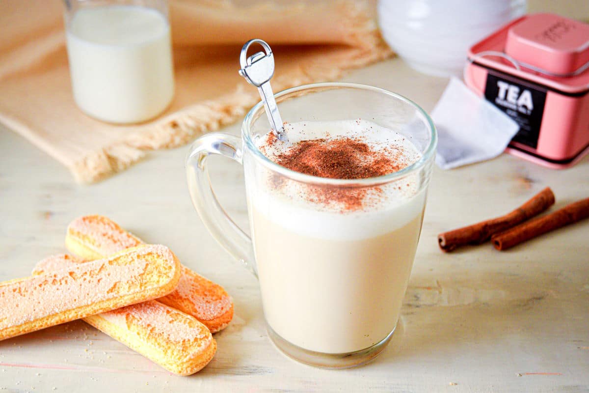 London fog tea latte in a clear glass mug with tea biscuits on the side.