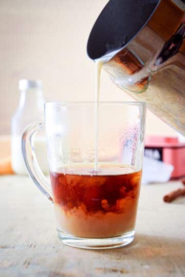 A clear glass mug of Earl Grey tea with steamed milk.