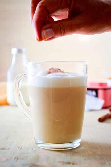 A clear glass mug of London Fog with frothed milk and cinnamon powder.