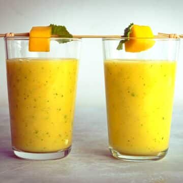 Mango pineapple smoothie in two glasses with skewered mango on top.