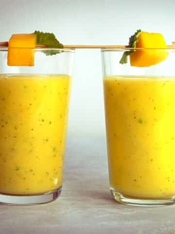 Mango pineapple smoothie in two glasses with skewered mango on top.