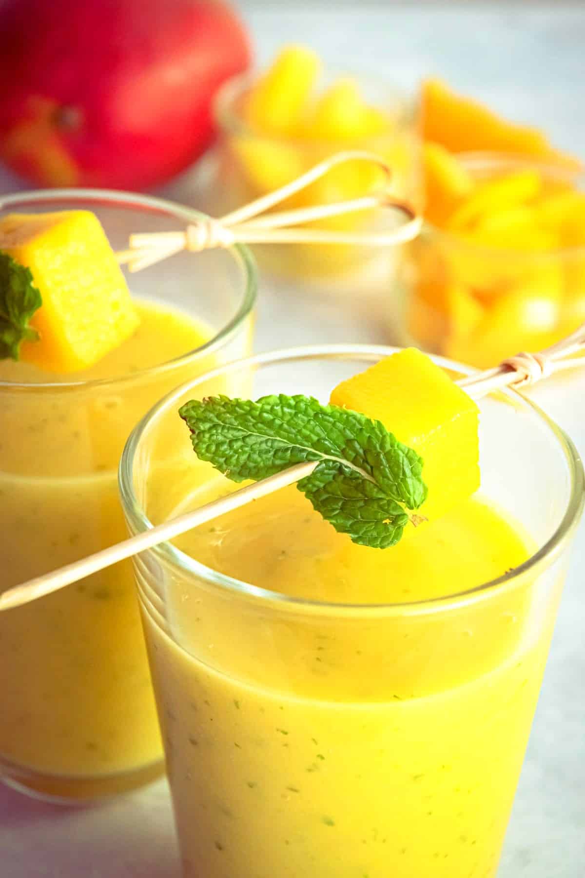 Mango pineapple smoothie in glass with mango skewer.