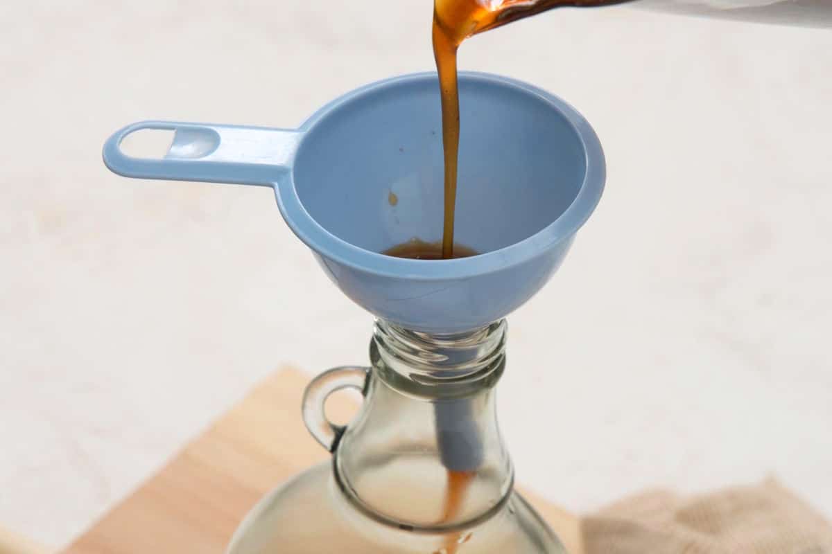 Caramel syrup getting poured through funnel into syrup jar.