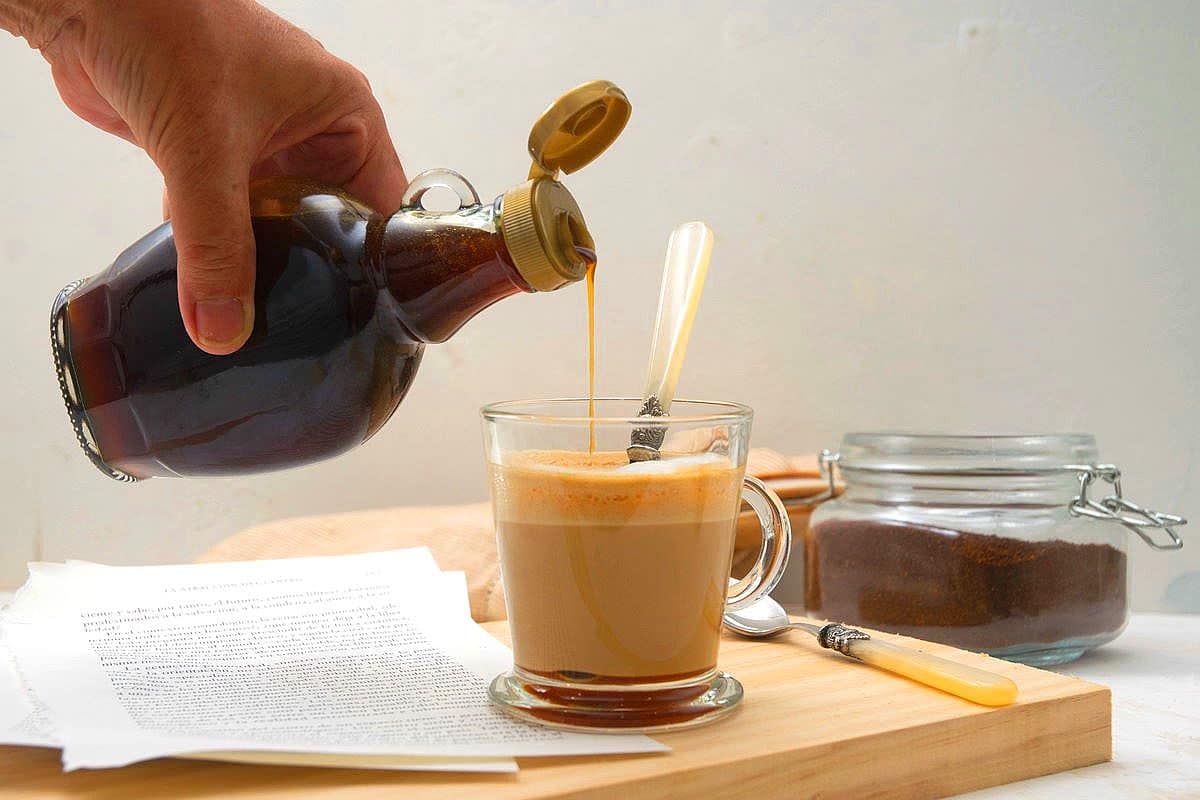 Caramel syrup pouring from bottle into coffee mug.