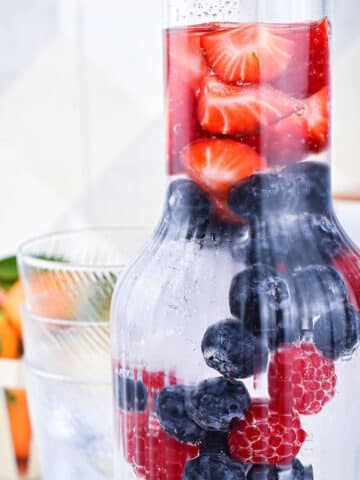 Fruit infused water with berries in glass pitcher.