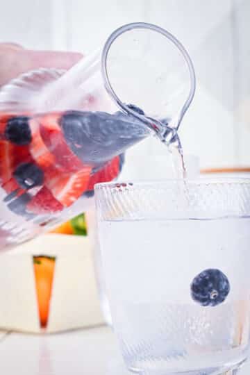 Fruit infused water in pitcher, pouring into glass.