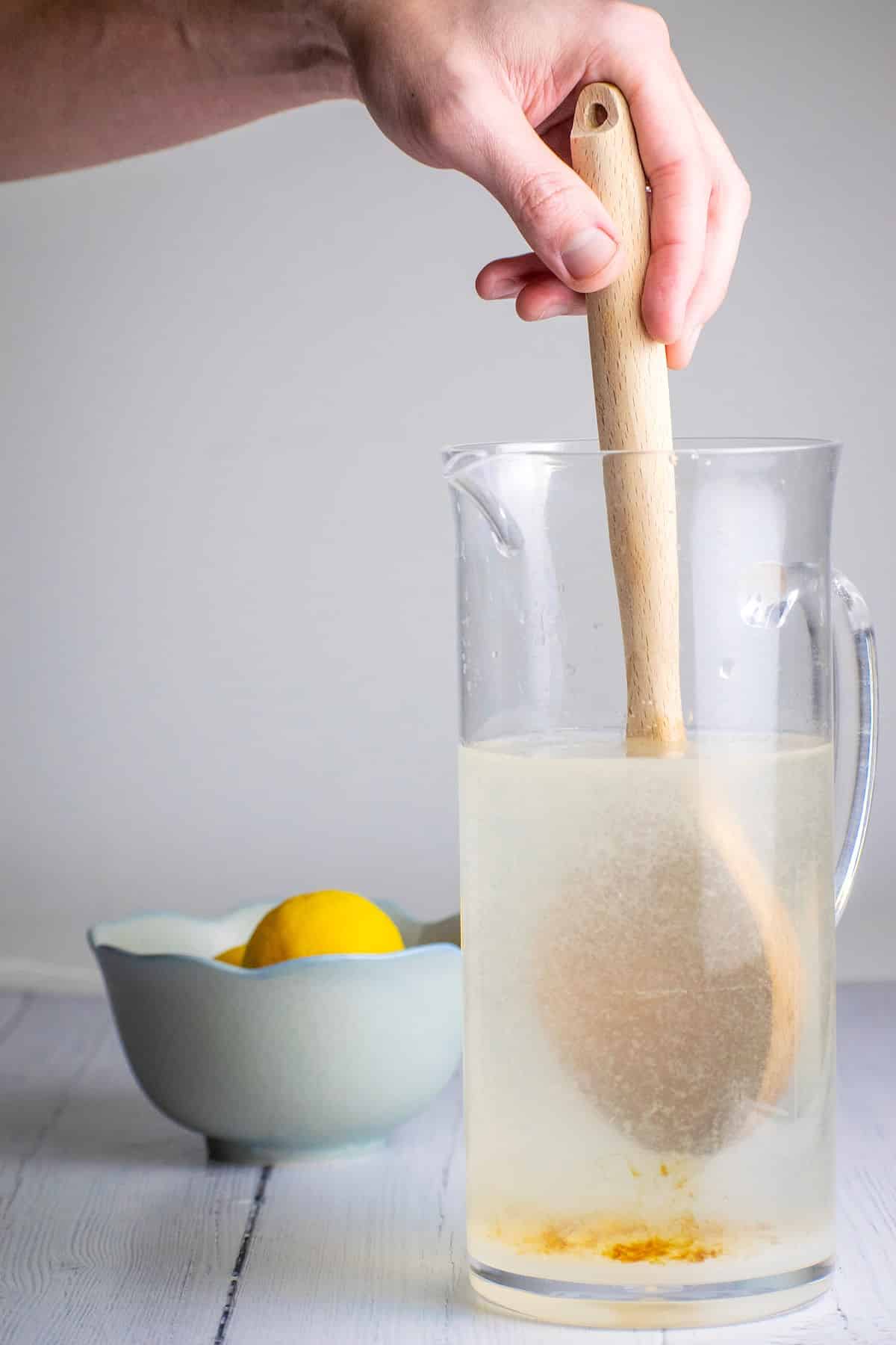Wooden spoon mixing lemonade in pitcher.