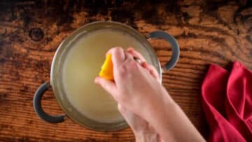 Hands squeezing lemon juice over pot of milk.
