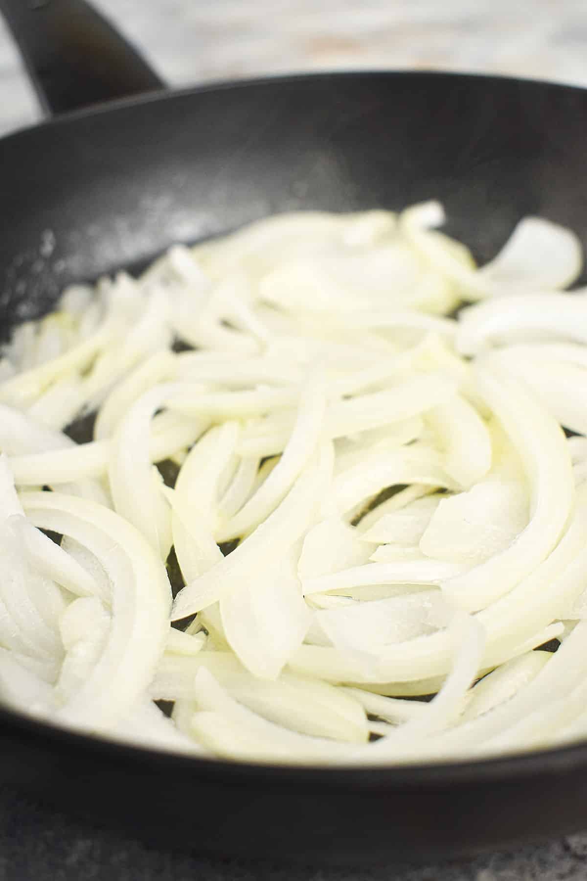 Sliced onions cooking in frying pan.