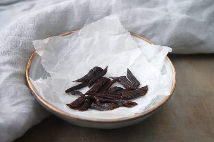 Vanilla beans cut into pieces on parchment.