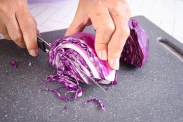Red cabbage shredded with knife on cutting board.