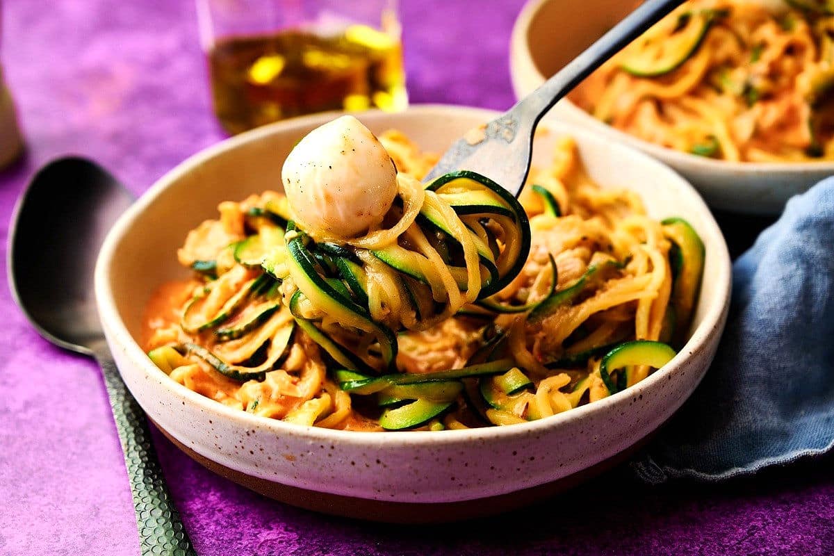 Zucchini noodles in bowl with bocconcini and fork.