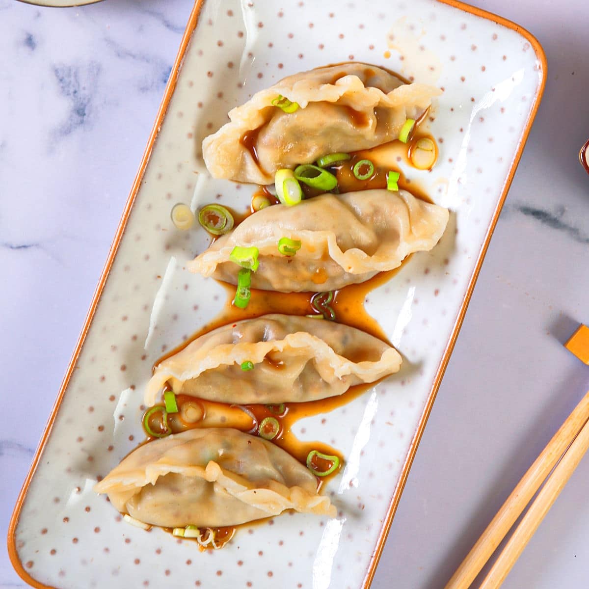 Kimchi dumplings with savory sauce and green onions in dish.
