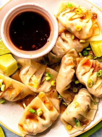 Kimchi dumplings arranged on plate with dipping sauce.