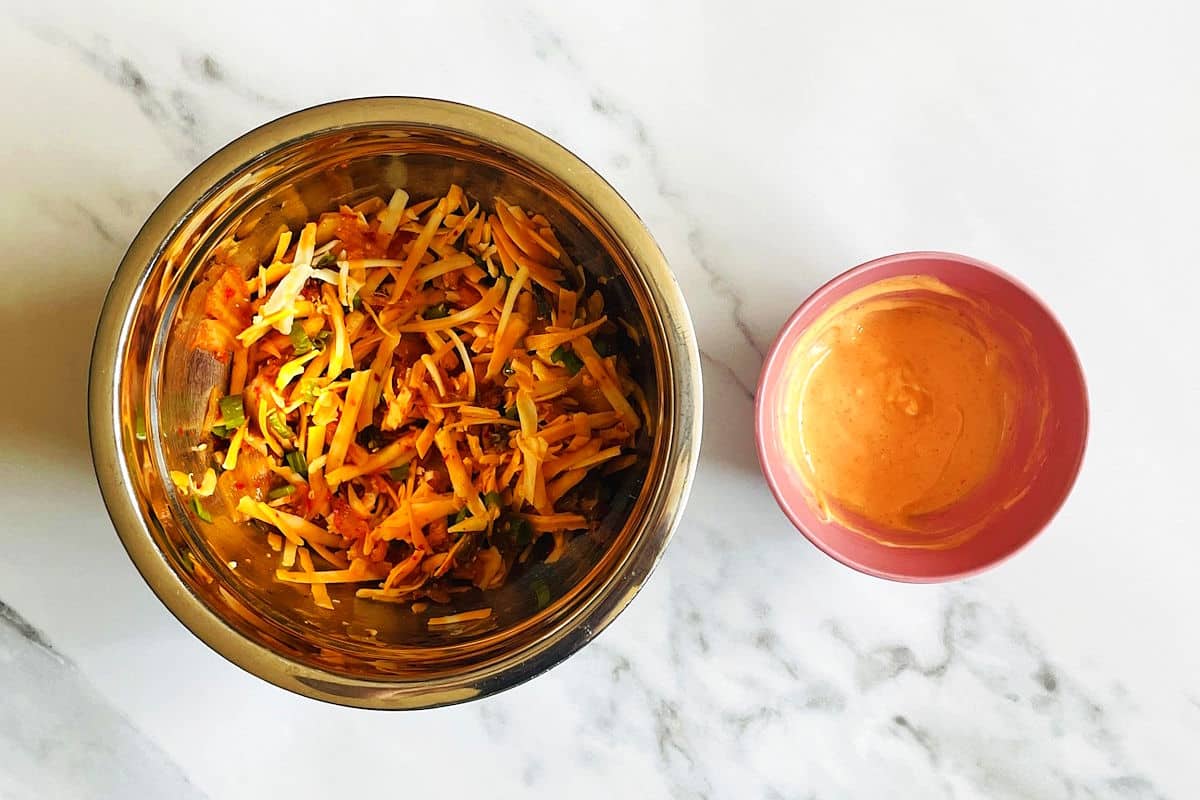 Kimchi grilled cheese filling in a bowl with sriracha mayo on the side.