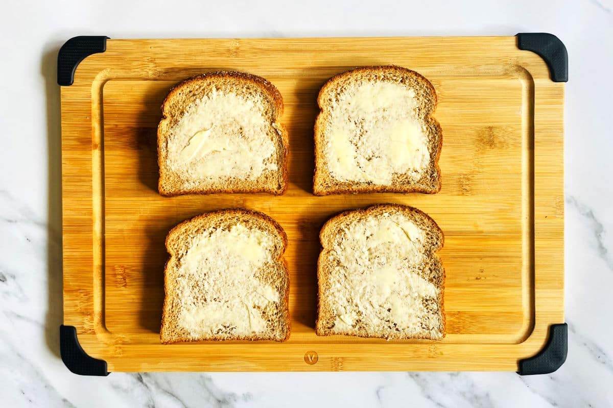 4 slices of bread with butter on cutting board.