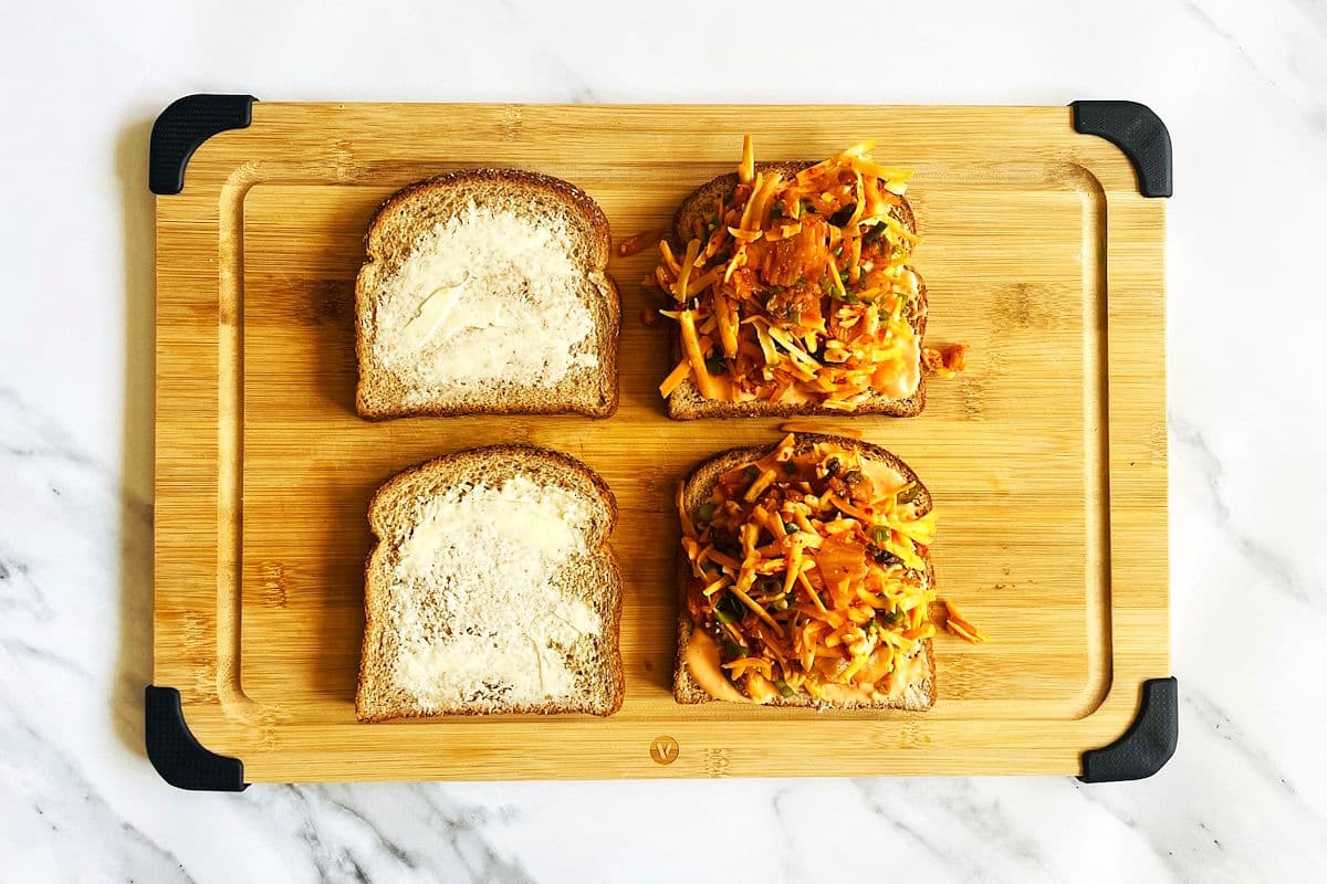 Bread slices with butter and kimchi cheese filling on cutting board.