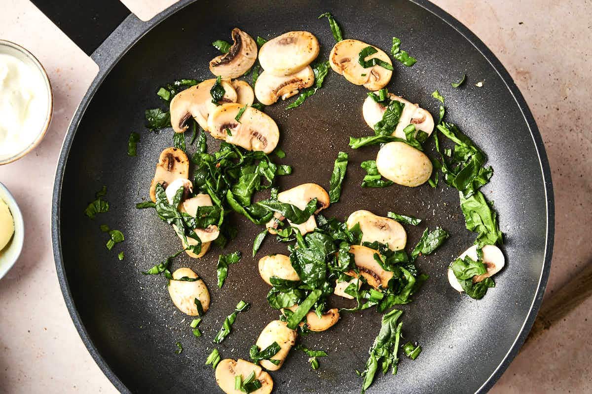 Sliced spinach and mushrooms in skillet.