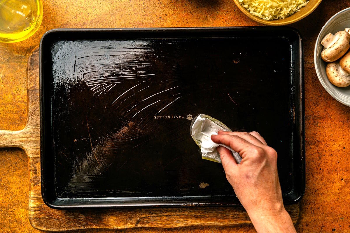 Woman's hand greasing a baking sheet.