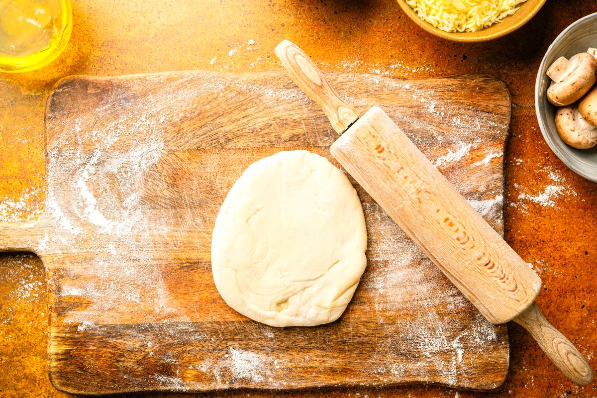 Pizza dough on wooden board wth rolling pin.