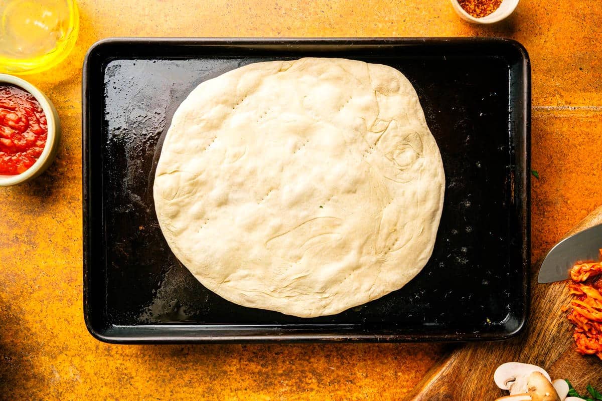 Pizza dough parbaked on baking sheet.