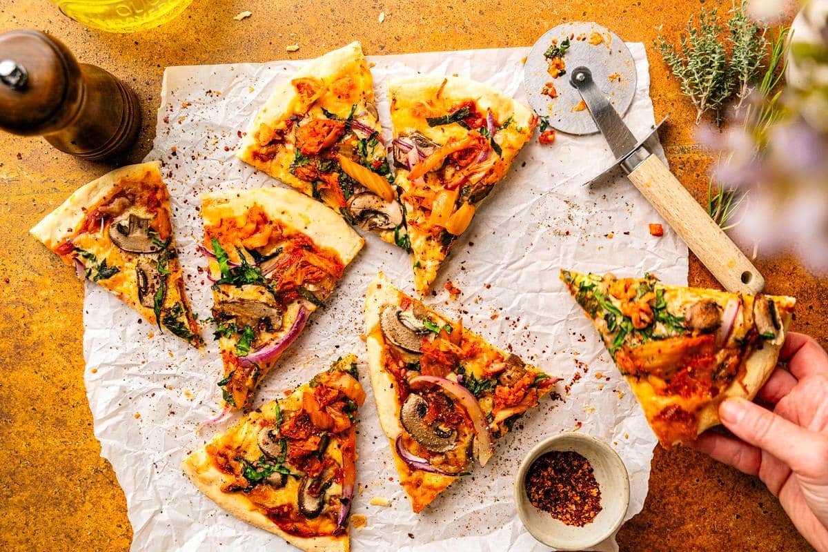 Kimchi pizza sliced on parchment with pizza slicer on the side.