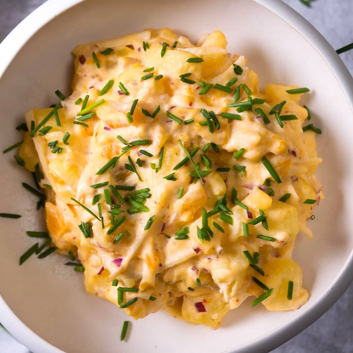 Kimchi potato salad with chives in white bowl.