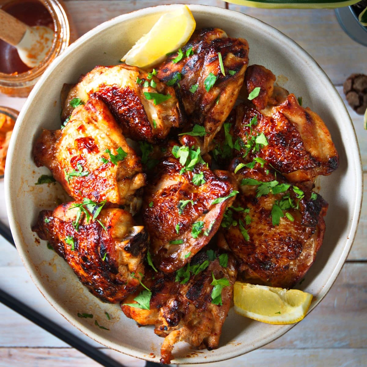 Korean kimchi chicken thighs in bowl with lemon wedges.