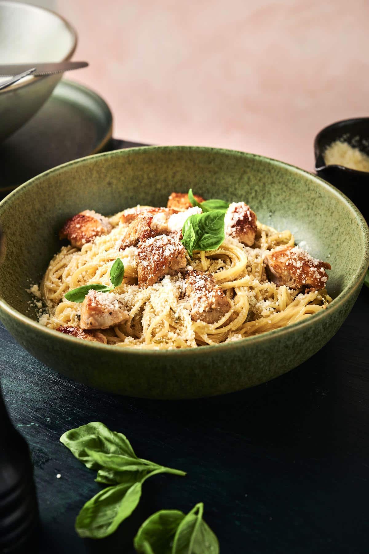 Lemon basil pasta with cubes of chicken breast in green bowl.