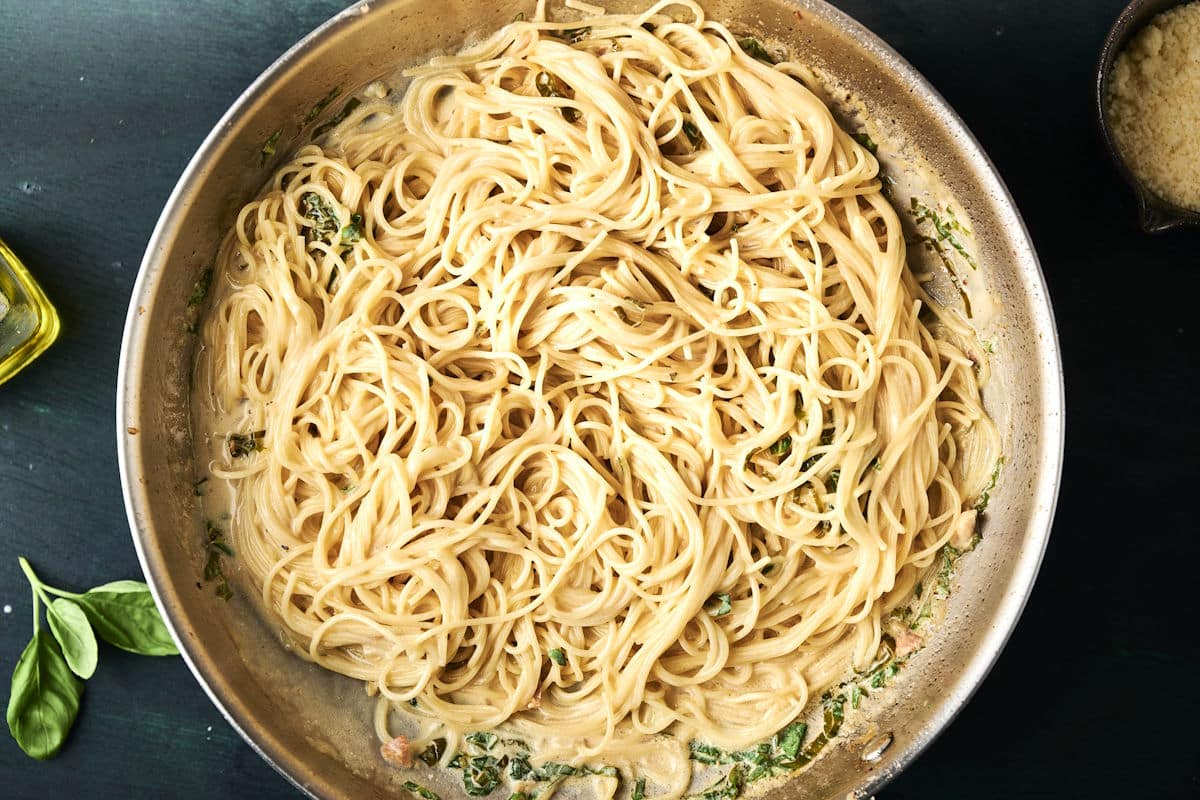 Angel hair noodles with creamy lemon basil sauce in pan.
