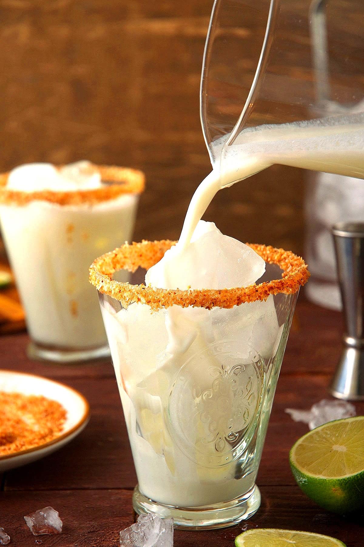 Toasted coconut rimmed glass with ice and lime cremosa pouring into it.