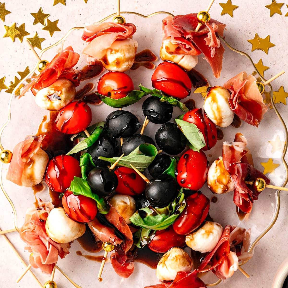 Mini caprese skewers arranged on plate with NYE decorations on the side.