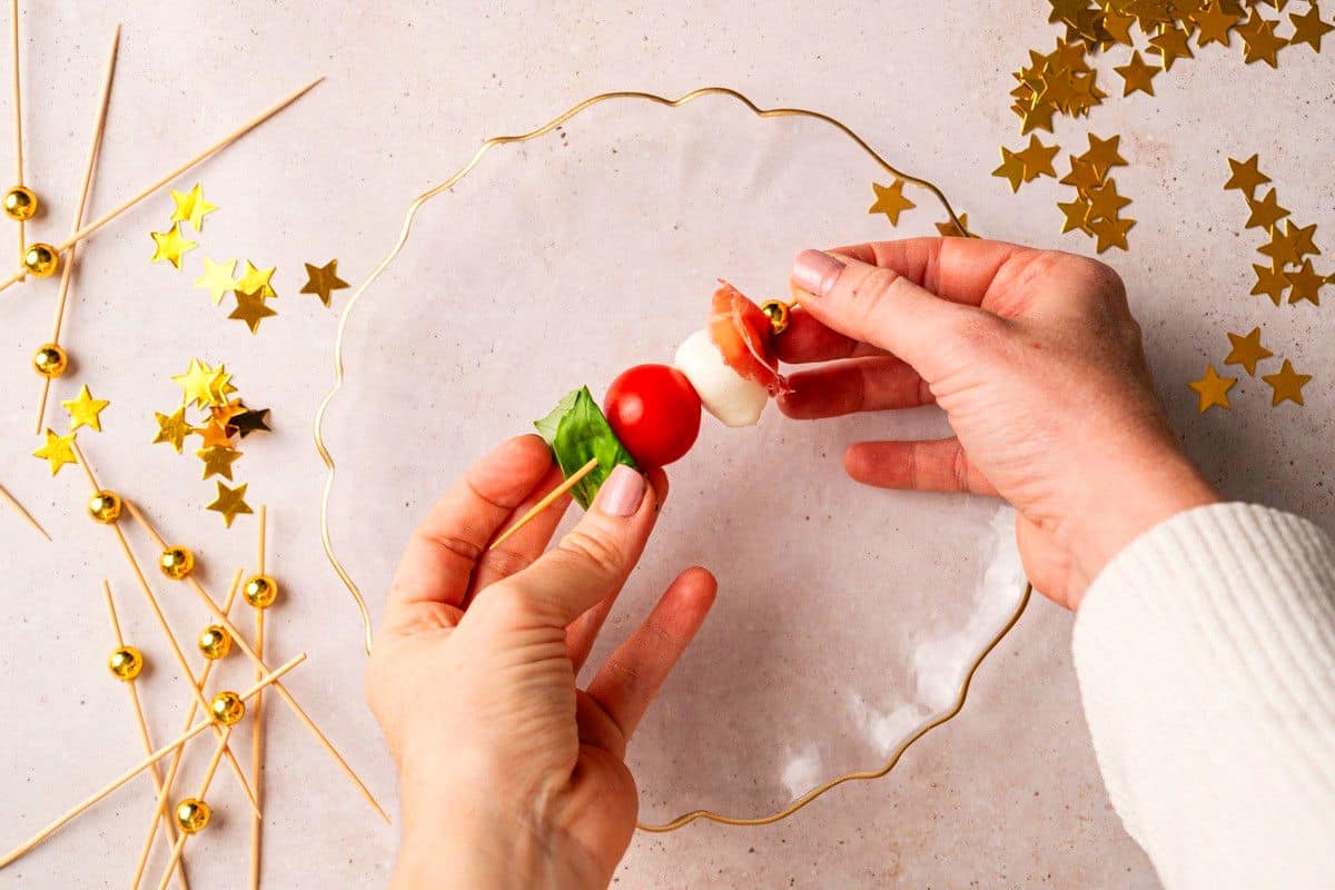 Woman's hands assembling a mini caprese skewer.