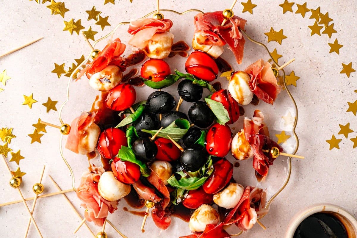 Mini caprese skewers drizzled with balsamic vinegar reduction on clear serving dish.