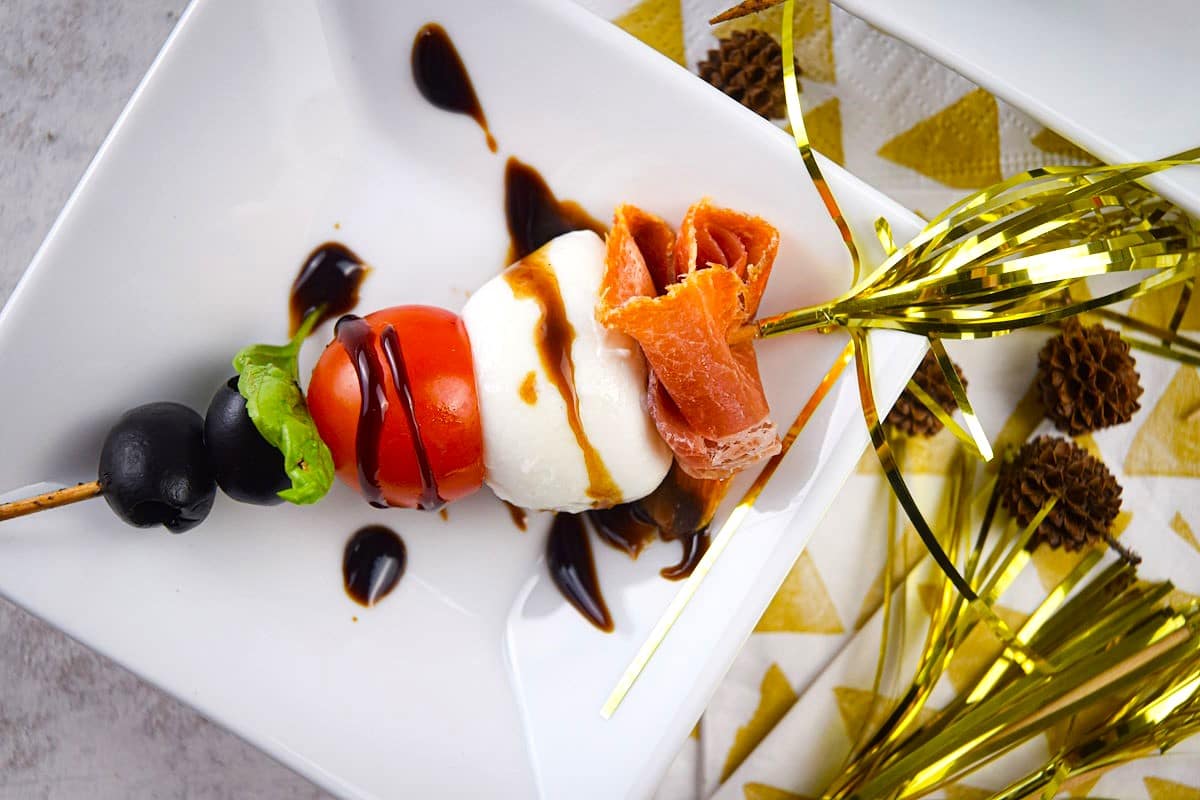 Mini caprese skewer on small white plate with New Year's Eve decoration.