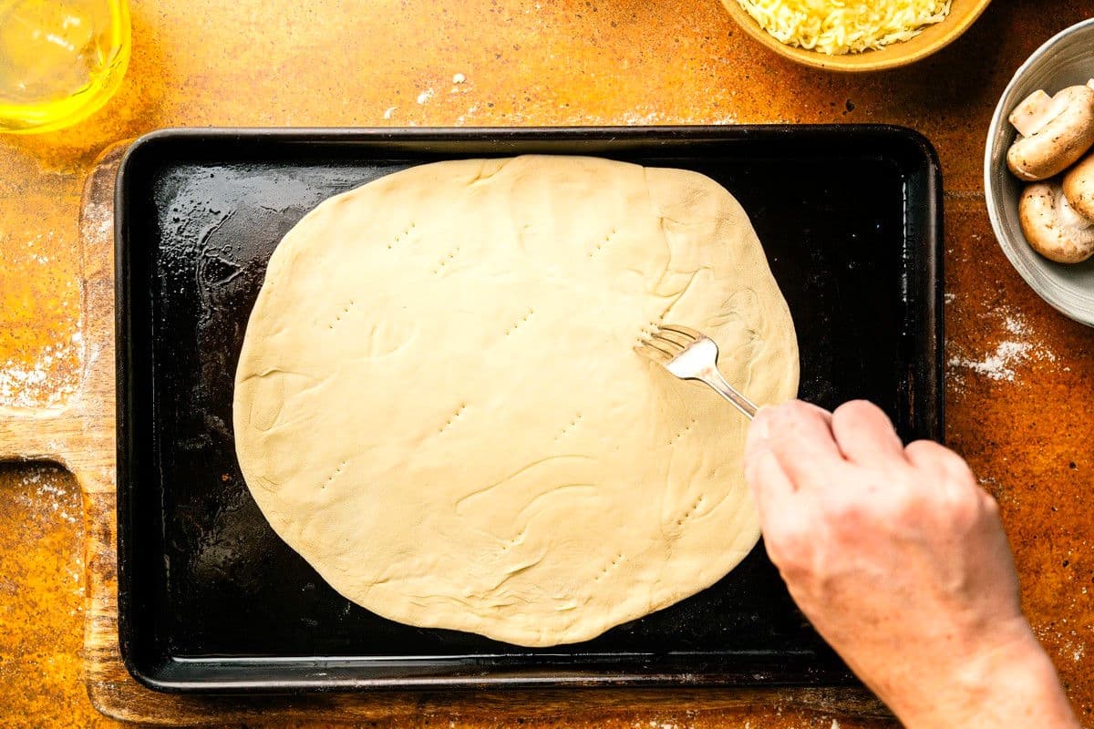 Woman's hand with a fork pricking pizza dough.