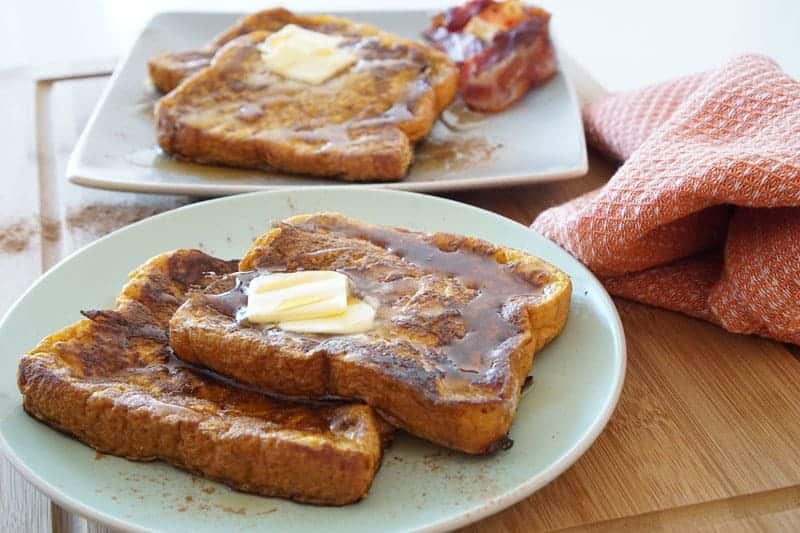 Pumpkin French toast with slabs of butter on white plates.