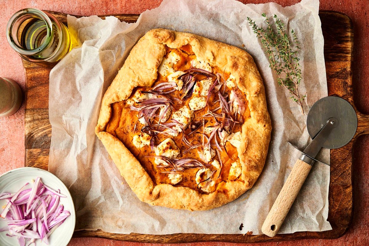 Baked savory pumpkin galette on sheet pan with pizza cutter on the side.