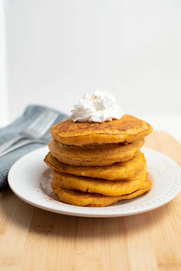 Pumpkin pancakes stacked on white plate with whipped topping.