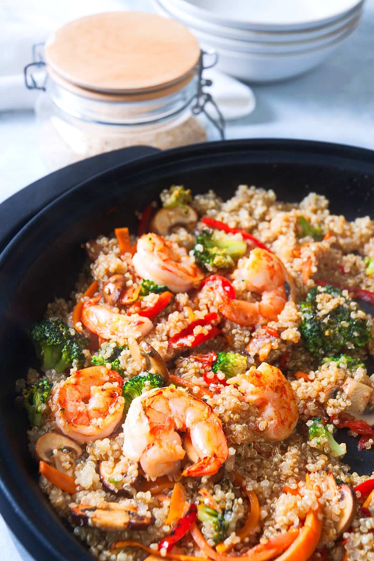 Shrimp and quinoa stir fry in skillet with quinoa in the background.
