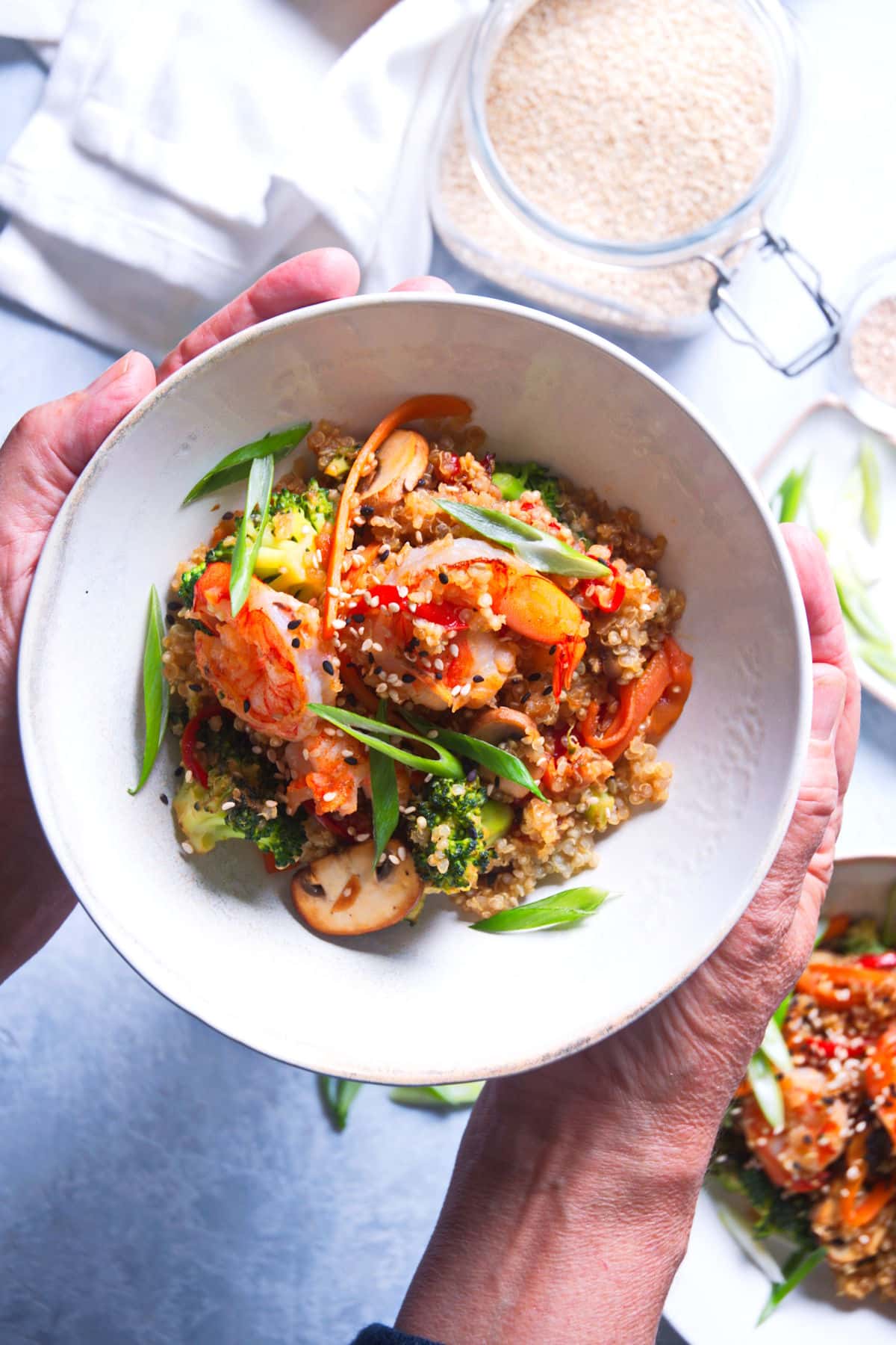Quinoa stir fry in white bowl held by woman's hands.