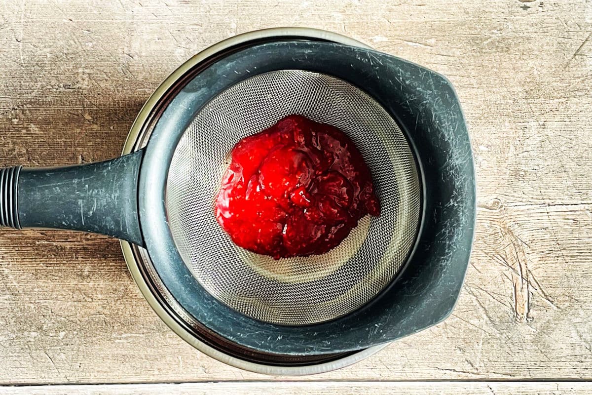 Raspberry coulis straining through fine mesh strainer.