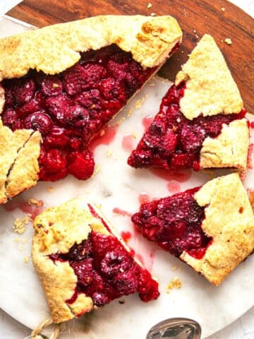 Raspberry galette on marble and wooden cutting board.