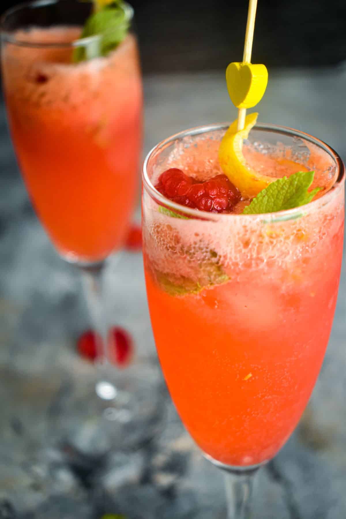 Raspberry twist cocktail in a champagne glass with a yellow heart skewer.