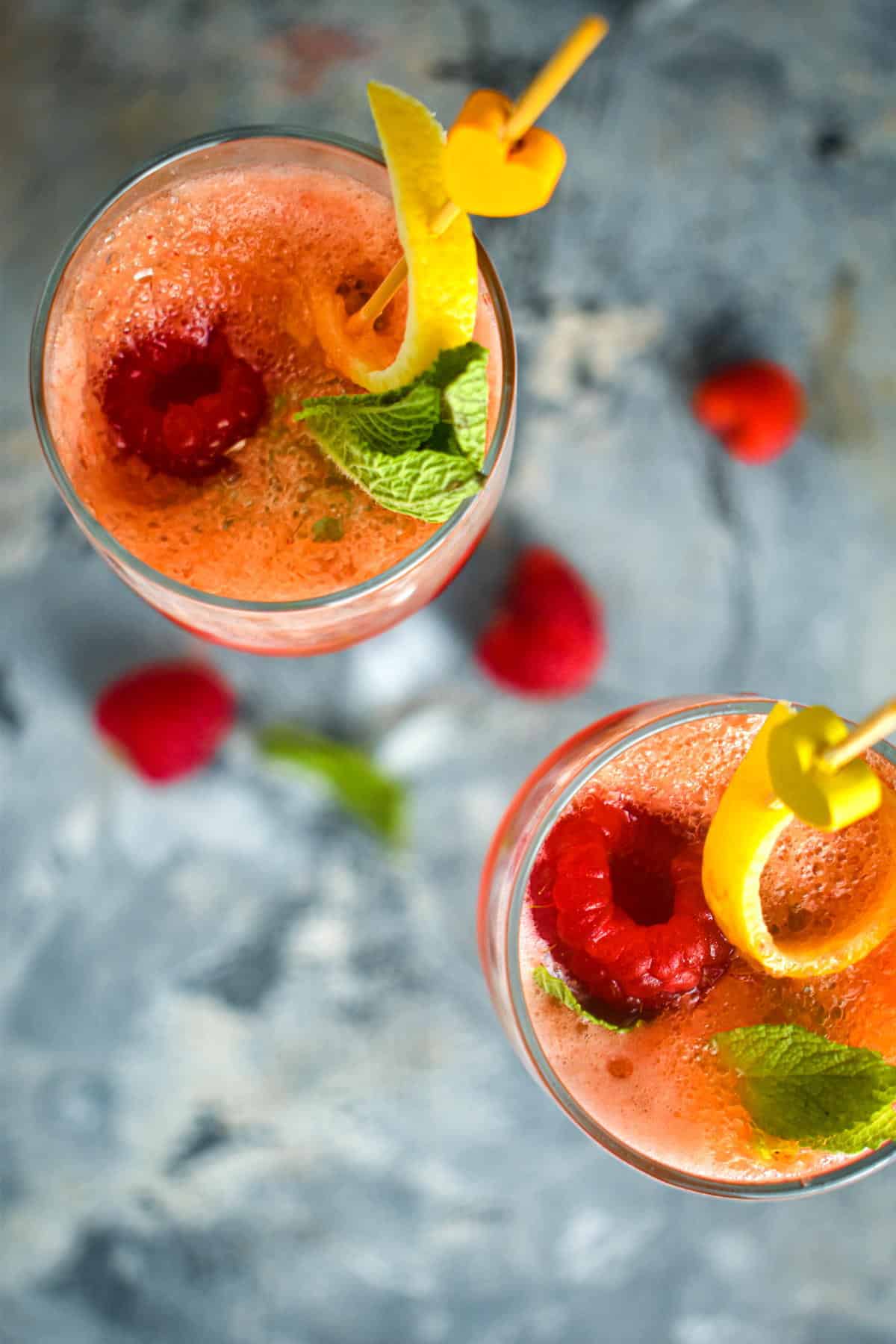 Top view of raspberry twist cocktail in champagne glasses with a lemon twist and mint leaf.