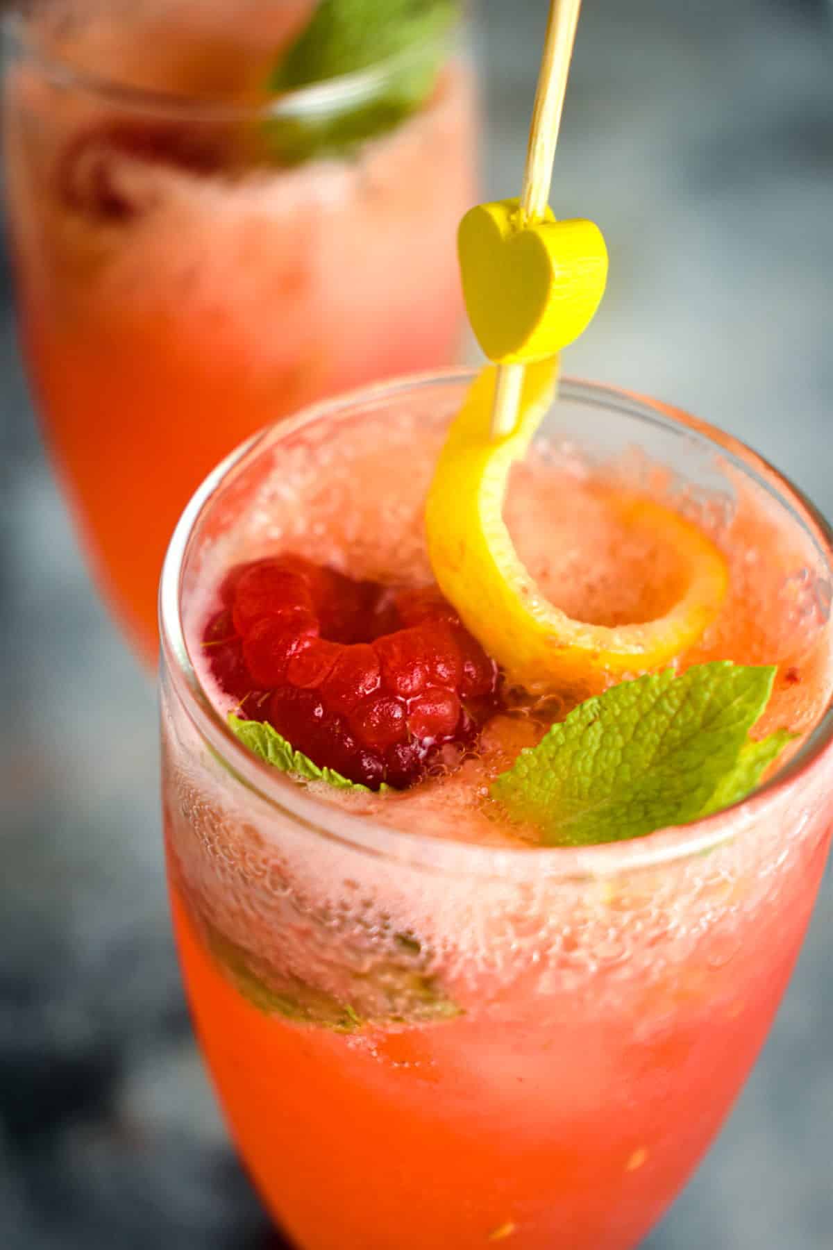 Raspberry twist cocktail in champagne glass with a lemon twist and mint leaf.